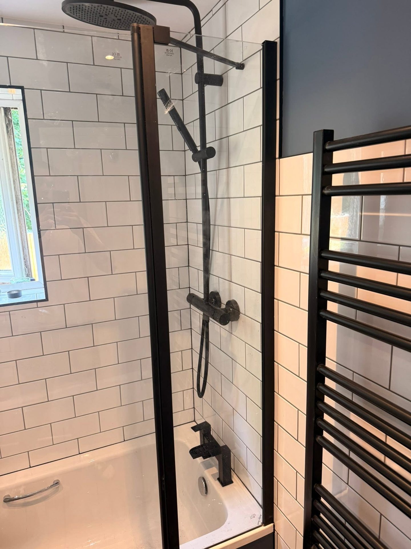 Matt black shower valve and riser fitted onto white metro tiling in a new bathroom installation