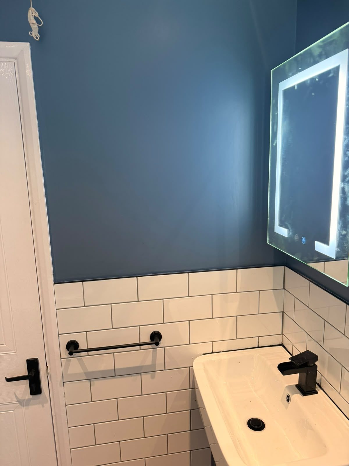 Bathroom vanity unit with black handles, white metro tiling and a blue feature wall after a full refit