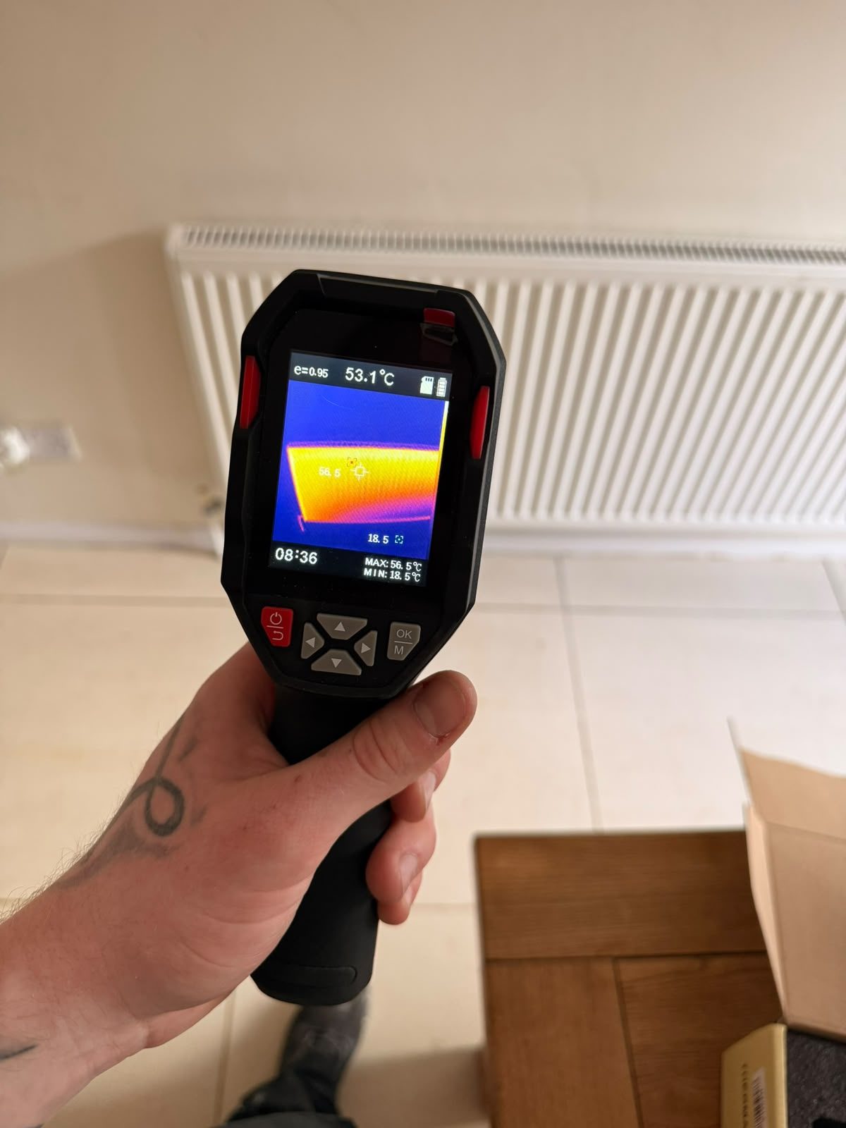 Engineer using a thermal imaging camera to survey a radiator and pipework while tracing a hidden leak