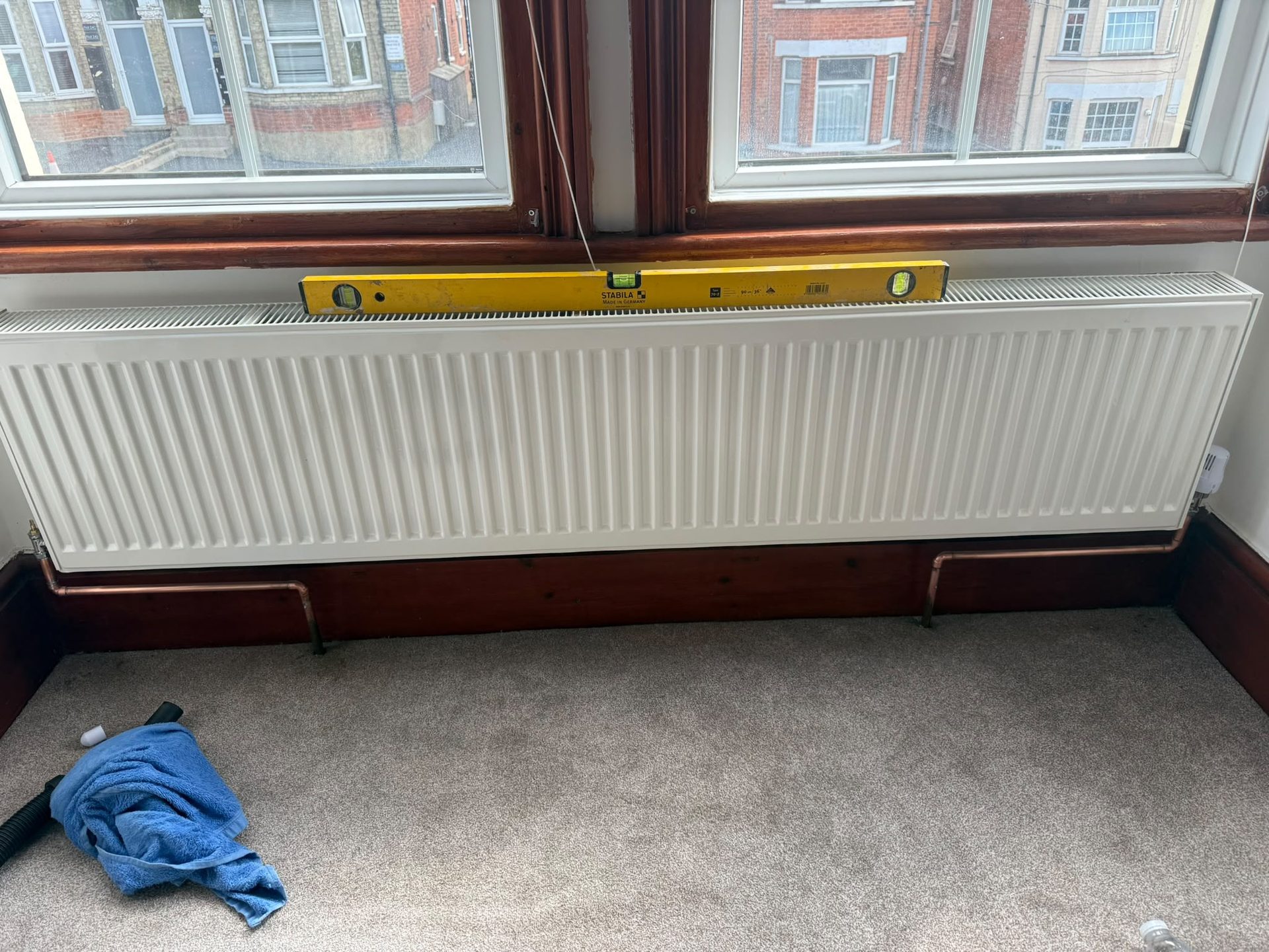 New white panel radiator fitted under a window and levelled during installation